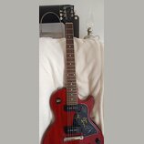 Červená elektrická kytara s tmavým hnedým hmatníkem. Na hlavě je bílé logo Gibson a nápis Les Paul. Černý plechtrguard obsahuje několik podpisů zlato…