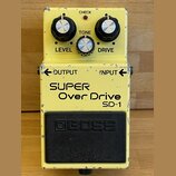 Žlutý kytarový efekt s nápisy SUPER Over Drive a SD-1. Na horní straně jsou tři ovládací knoflíky s popisky LEVEL, TONE a DRIVE a kontrolka CHECK. V…