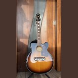 Akustická kytara s vyřezem (cutaway) v provedení sunburst. Na hlavě je nápis Epiphone a na hradle se nachází štítek s textem GUARANTEED Lifetime Warr…