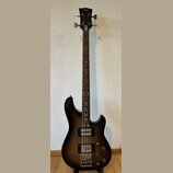 Tmavně hnědá elektrická basová kytara s tmavým hnedým hnedým dřevěným hmatníkem. Na hlavě nástroje je nápis Superstar. Kytara má dva humbuckery, tři…