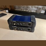 Dvě pasivní DI boxy značky PROEL, model DB1+P PASSIVE D.I.BOX. Horní kus má modré kovové tělo s žebrovaným povrchem a černé plastové kryty na koncích…