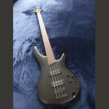 Černá elektrická basová kytara s tmavým povrchem a hnědým hmatníkem. Nástroj má dva snímače typu humbucker a tři ovládací knoflíky. Na hlavě je vidit…
