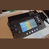 Černý digitální mixovací pult s dotykovým displejem, na kterém je zobrazeno míchací rozhraní s barevnými faderem. Na horní straně je nápis ALLEN&HEAT…