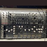 Fotografie zachycuje modulární syntetizátor v racku. Horní řada obsahuje moduly s nápisy Endorphine, COSMOTRONIC, Queen Of Pentacles a BLACK JOYSTICK…