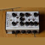 Bílý kytarový zesilovač s nápisem SIMPLIFIER MKII ZERO WATT REVERB STEREO AMPLIFIER. Zařízení obsahuje několik černých otočných potenciometrů a přepí…