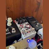 Detailní záběr na několik kytarových efektů v pedalboardu. Uprostřed je bílý pedál s červenobílou grafikou, který nese nápisy ratio, program a v doln…