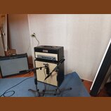 Fotografie zachycuje dva kytarové zesilovače a jednu basovou hlavu v interiéru. Vlevo stojí černý kombo zesilovač s nápisem Fender Custom Deluxe. Upr…
