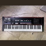 Černý syntetizátor s červeným horním panelem. Na levé straně je bílý nápis Roland a model JX-3P, pod kterým je text PROGRAMMABLE PRESET POLYPHONIC SY…