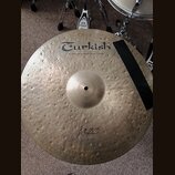 Kulatý mosazný činel s kovaným povrchem. Na horní části je černý nápis Turkish a pod ním text handmade cymbals from Turkey. Ve spodní části je rukopi…
