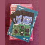 Fotografie zobrazuje červenobílý karton s nápisem YAMAHA PLG150-AN Plug-in Board, modrou obálku s logem YAMAHA a čtyři 3,5" diskety. Na disketách je…