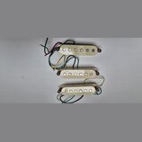 Tři krémově bílé snímače pro elektrickou kytaru s šesti kovovými póly. Každý snímač má v levé části nápis NPS a je vybaven připojovacími vodiči v růz…