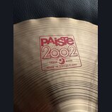 Detail činely z mosazi s koncentrickými rýhami. Na povrchu je červený nápis PAiste 2002, pod kterým je v rámečku text TRADE MARK a MADE IN SWITZERLAN…