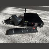 Černý audio přístroj s knoflíkem a anténou, na kterém jsou nápisy TOPPING a DX3Pro. Vedle přístroje je černý napájecí adaptér s kabelem a černý dálko…