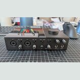 Černý zvukový interface s nápisem KOMPLETE AUDIO 6 na horní straně. Přední panel obsahuje dva kombinované vstupy (IN 1, IN 2), přepínače LINE/INST a…