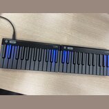 Černá elektronická klaviatura tvořená dvěma spojitými moduly. Na horní hraně obou částí je bílý nápis LUMI a ovládací tlačítka. Některé klávesy jsou…