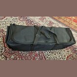 Černý textilní pouzdro (gig bag) obdélníkového tvaru s dvěma nosními popruhy. Povrch materiálu vykazuje drobné nečistoty a opotřebení. Na pouzdře nej…