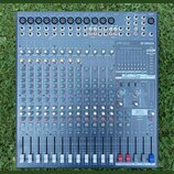 Šedý mixovací pult značky YAMAHA s označením modelu EMX5016cF. Zařízení obsahuje více vstupních kanálů s posuvníky, řadu otočných knoflíků v různých…
