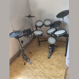 Elektronická bicí souprava s černým rámem a bílými bubnovými plochami. Souprava obsahuje pět padů, tři činely a ovládací modul s nápisem Roland. K sa…