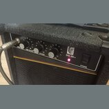 Černý kytarový kombo zesilovač s texturovaným povrchem. Na ovládacím panelu jsou tři černé otočné knoflíky s popisky TUBE STACK®, VOLUME a EQ, červen…