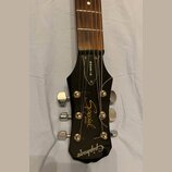 Detail hlavy černé kytary s hnedým hmatníkem. Na hlavě jsou bílé nápisy „GIBSON“, „Special MODEL“ a logo „Epiphone“. Jsou vidět šest chromovaných lad…