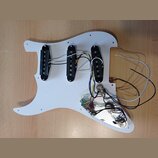 Bílá pickguard pro elektrickou kytaru s třemi černými snímači typu single-coil. K snímačům vedou bílé a černé vodiče, které jsou připojeny k elektron…