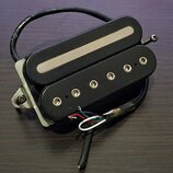 Černý humbucker s dvěma cívkami a kovovým krytem v horní části. Spodní cívka má šest viditelných polových šroubů. Nástroj je umístěn na kovové základ…