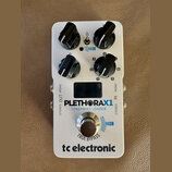 Bílý kytarový efekt s nápisy PLETHORAX1 a TONEPRINT LOADER. Na spodní části je logo tc electronic a nápis TRUE BYPASS. Zařízení má čtyři černé otočné…