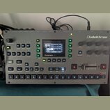 Stříbrný sampler s nápisem Elektron a Octatrack MKII. Zařízení obsahuje displej, několik ovládacích knoflíků, tlačítka s různými funkcemi a v dolní č…
