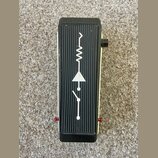Kytarový efekt v černé barvě s žebrovaným povrchem. Na horní straně je bílý symbol připomínající elektronickou schéma s vlnovkou, trojúhelníkem a pře…