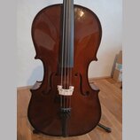 Hnědý smyčkový nástroj, pravděpodobně violoncello, s lakovaným povrchem. Na těle jsou vidět f-otvory, světlá dřevěná kobylka a černý strunník. Nástro…