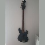 Tmavě šedá elektrická basová kytara s hnědým hmatníkem. Na hlavě je svisle napsáno „proxima t-bass“. Tělo nástroje vykazuje známky opotřebení v podob…