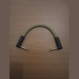 Kabel s úhlovými 6,3mm konektory v barvě zlata. Kabel má pletený obal v béžové barvě a černé gumové chrániče u konců. Na jednom z chráničů je nečitel…