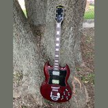 Kytara s tmavě červeným lakem a černým pickguardem, opřená o kmen stromu. Na hlavě je žlutý nápis "Lancer". Nástroj má dva humbuckery, tři ovládací k…