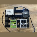 Na černém pedalboardu jsou umístěny čtyři efekty a napájecí zdroj. V horní části je bílý zdroj s nápisem POWER PLANT Junior a pětivstupním rozdělením…