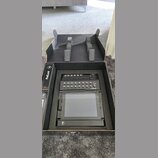 Černý elektronický přístroj s ovládacími prvky a displejem umístěný v originální kartonové krabici s pěnovými vložkami. Na horní části přístroje je n…