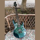 Kytara s tmavě zeleným kovovými lakem a hnědým hmatníkem. Na hlavě je bílý nápis "Schecter". Nástroj má dva humbuckery a fixační most. Povrch laku je…