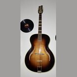 Akustická kytara s polodubovou konstrukcí v tmavě hnědém sunburst provedení. Na těle jsou viditelné dva f-otvory a kovový most. Na hlavě nástroje je…