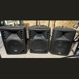 Tři černé plastové reproduktory s integrovanými úchopy z hnědé kůže. Krajní dva mají v dolní části logo RH SOUND, prostřední reproduktor má nápis AME…