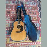 Akustická kytara s přírodním dřevem a černým plechtrem v modrém tvrdém pouzdře. Na hlavě nástroje je viditelné logo "Epiphone". Kytara i pouzdro vyka…