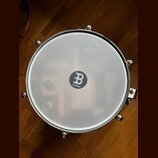 Fotografie zachycuje bílou bubenovou membránu s kovovým obručem. Uprostřed je černé kulaté logo s bílým symbolem „B“ a nápisem MEINL. Membrána je v č…