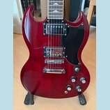 Červená elektrická kytara s černým pickguardem a hnedým hmatníkem. Nástroj má dva humbuckery, čtyři ovládací knoflíky a jeden přepínač. Na kytáře nej…
