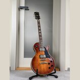Elektrická kytara s tvarem singlecut a povrchovou úpravou v hnědém sunburstu. Na hlavě je viditelné logo Gibson. Kytara má dva humbuckery, čtyři otoč…