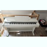 Bílé digitální piano s bílým stojanem a třemi pedály. Na hudebním stojanu je umístěno logo YAMAHA. Nástroj vykazuje čistý povrch bez viditelných pošk…