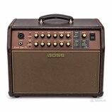 Hnědý akustický zesilovač s látkovou mřížkou a koženým úchem. Na předním panelu je nápis Acoustic Singer Pro a v centru mřížky logo BOSS. Ovbední pan…