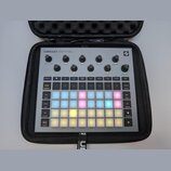 Šedý sampler Novation Circuit Rhythm v černém přepravním pouzdře. Horní část obsahuje osmi otočných ovladačů s popisky jako Master Volume, Start, Sto…