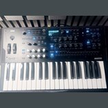 Šedý syntetizátor s klaviatura značky KORG, na jehož pravé straně je nápis wavestate. Přístroj disponuje displejem, několika posuvníky, otočnými knof…