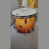 Kytarový nebo bubnový nástroj, konkrétně tom, s povrchem v oranžovém gradientu (sunburst). Na bláně je viditelný nápis EVANS a na korpusu kulatá nále…