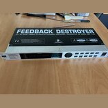 Stříbrný rackový procesor s nápisem FEEDBACK DESTROYER a označením MODEL DSP 1100. Na horní straně je logo BEHRINGER a varovné štítky s nápisy CAUTIO…