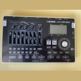 Stříbrnošedý digitální nahrávač s černým ovládacím panelem. Na horní části je nápis BOSS DIGITAL RECORDER BR-800 a LCD displej. Přístroj obsahuje něk…