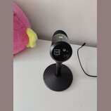 Černý mikrofon na kulatém stojanu. Na zadní straně je bílé logo VI a pod ním menší nečitelný nápis, dále jsou vidět konektory pro USB a jack. Horní č…